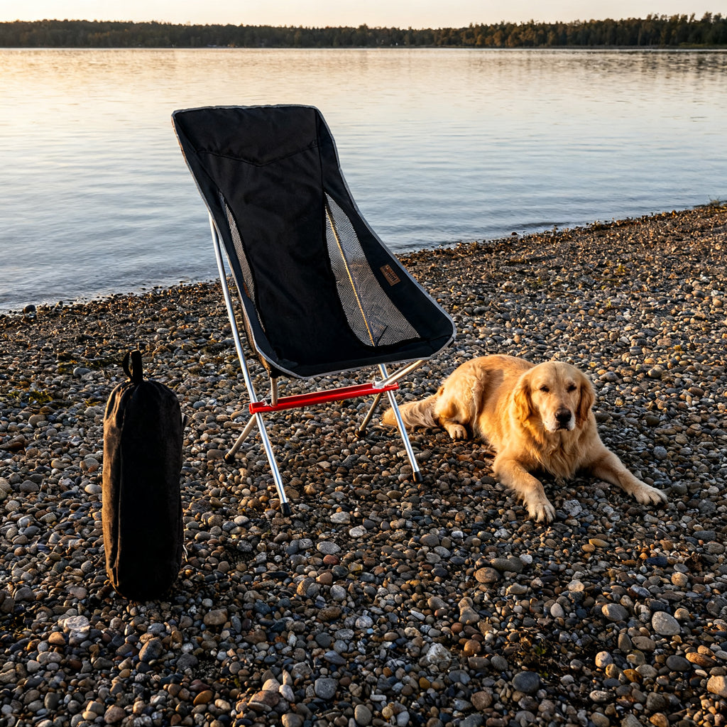Black Heightened Moon Chair on a pebble lake shore with a dog resting beside it