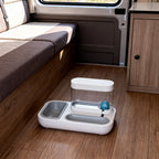 TrailPaw Auto Feeder on a camper van floor beside a dinette bench, showing its compact size